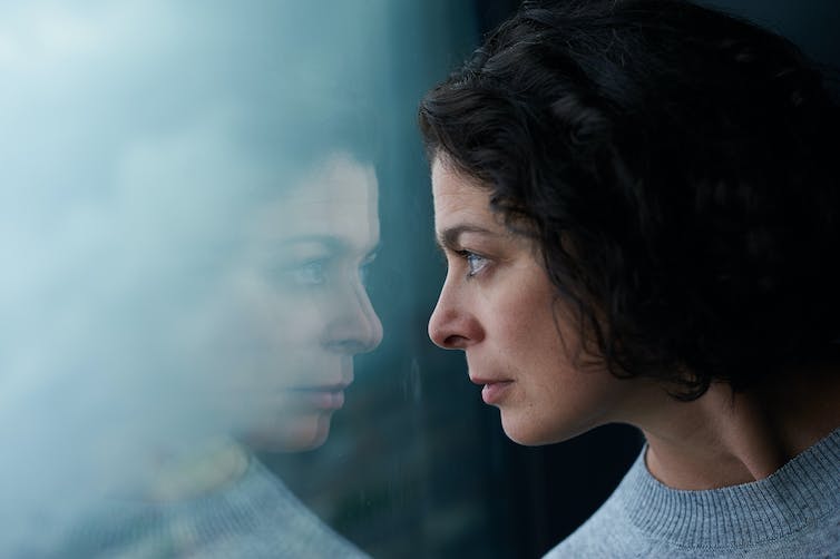 A woman looks at her reflection in a pane of glass.