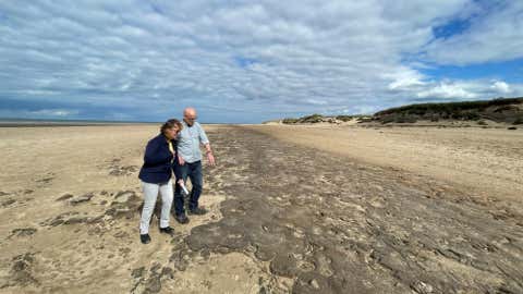 Dr Alison Burns and Professor Jamie Woodward from The University of Manchester inspecting 8500-year-old animal and human footprints in one of the Mesolithic mud beds at Formby.(Victoria Gill, BBC)